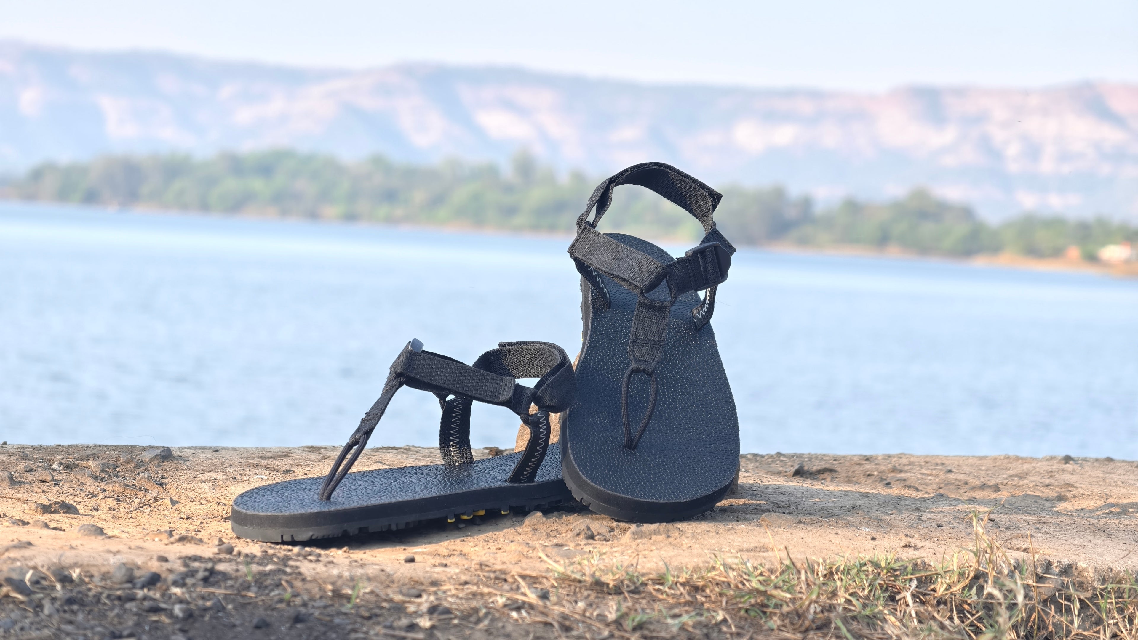 Black sandals on a stone surface with a scenic background of water and mountains.