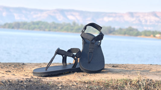 Black sandals on a stone surface with a scenic background of water and mountains.